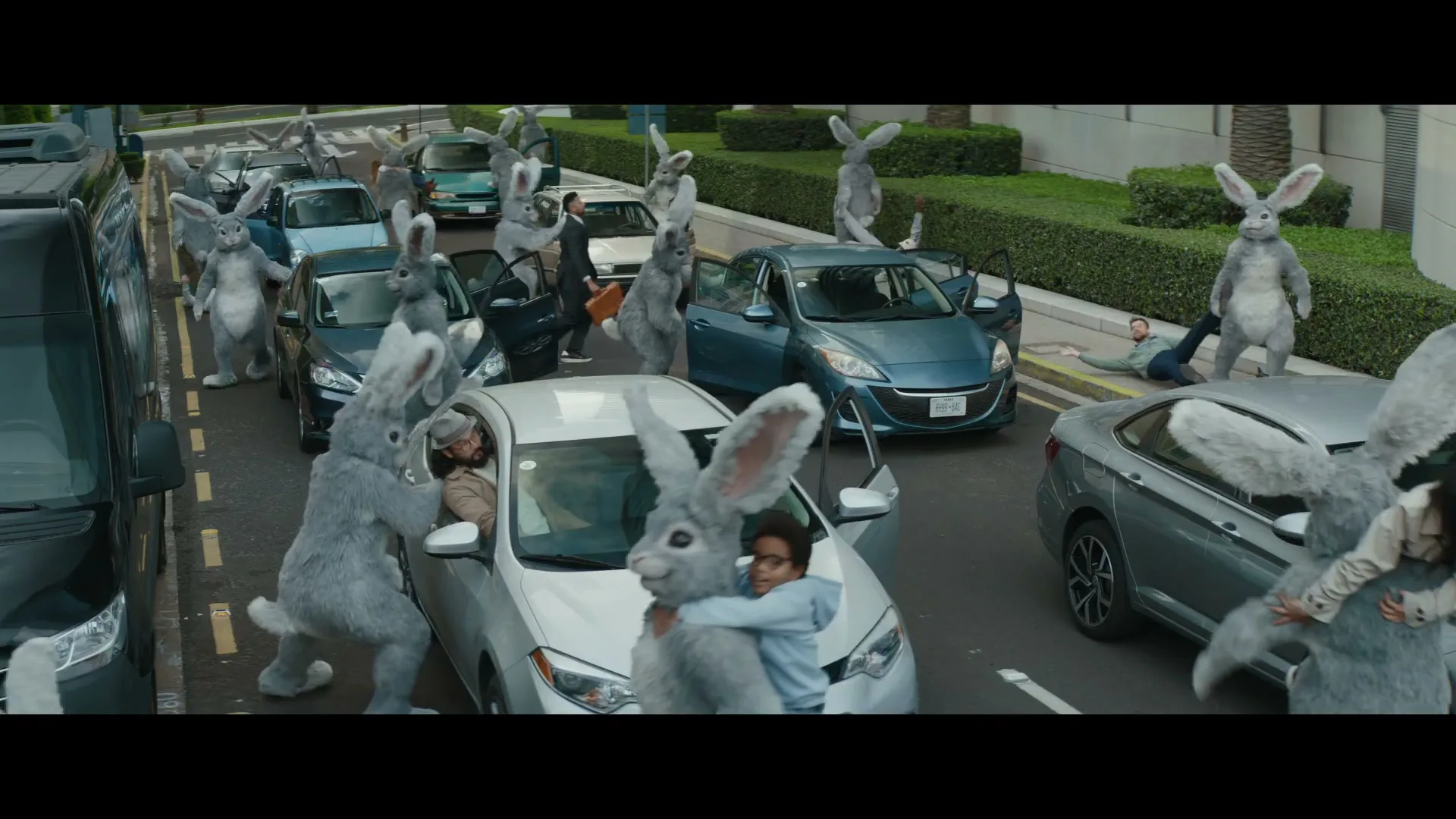 A chaotic scene unfolds on a city street as numerous people in rabbit costumes swarm cars, pulling out drivers and passengers.