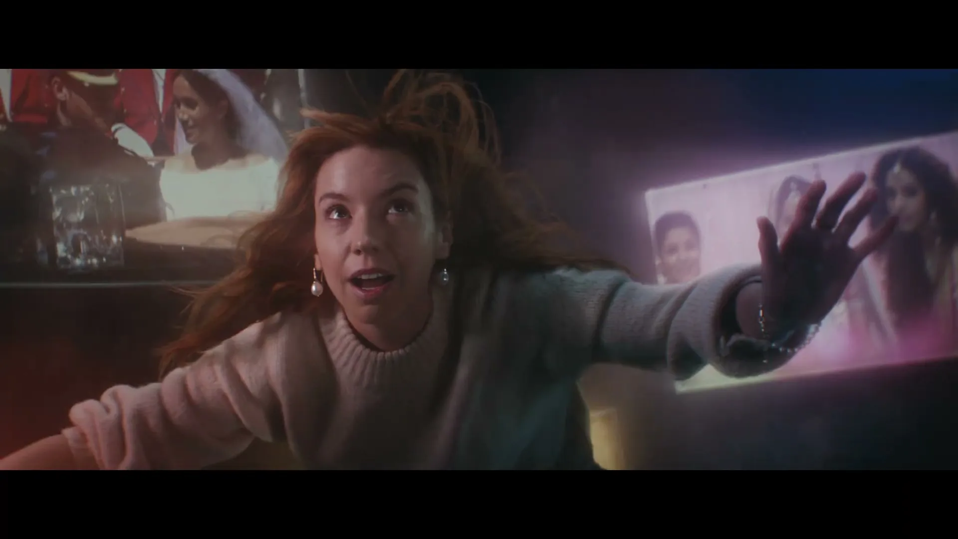 A young woman with red hair and a light sweater falls through a dark space, surrounded by floating images of people.