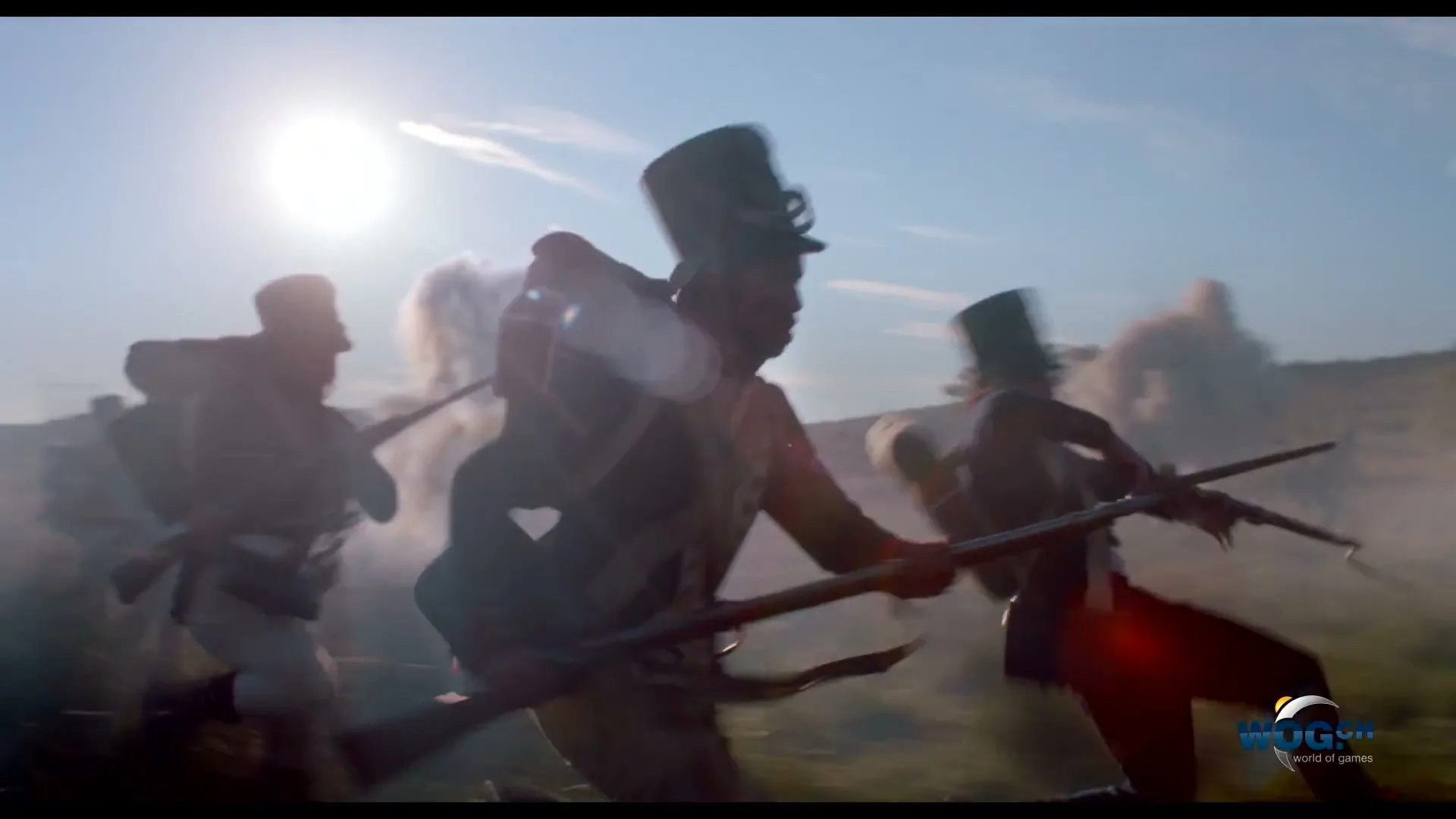 A group of soldiers in historical uniforms run across a battlefield with smoke and explosions in the background under a bright sun.