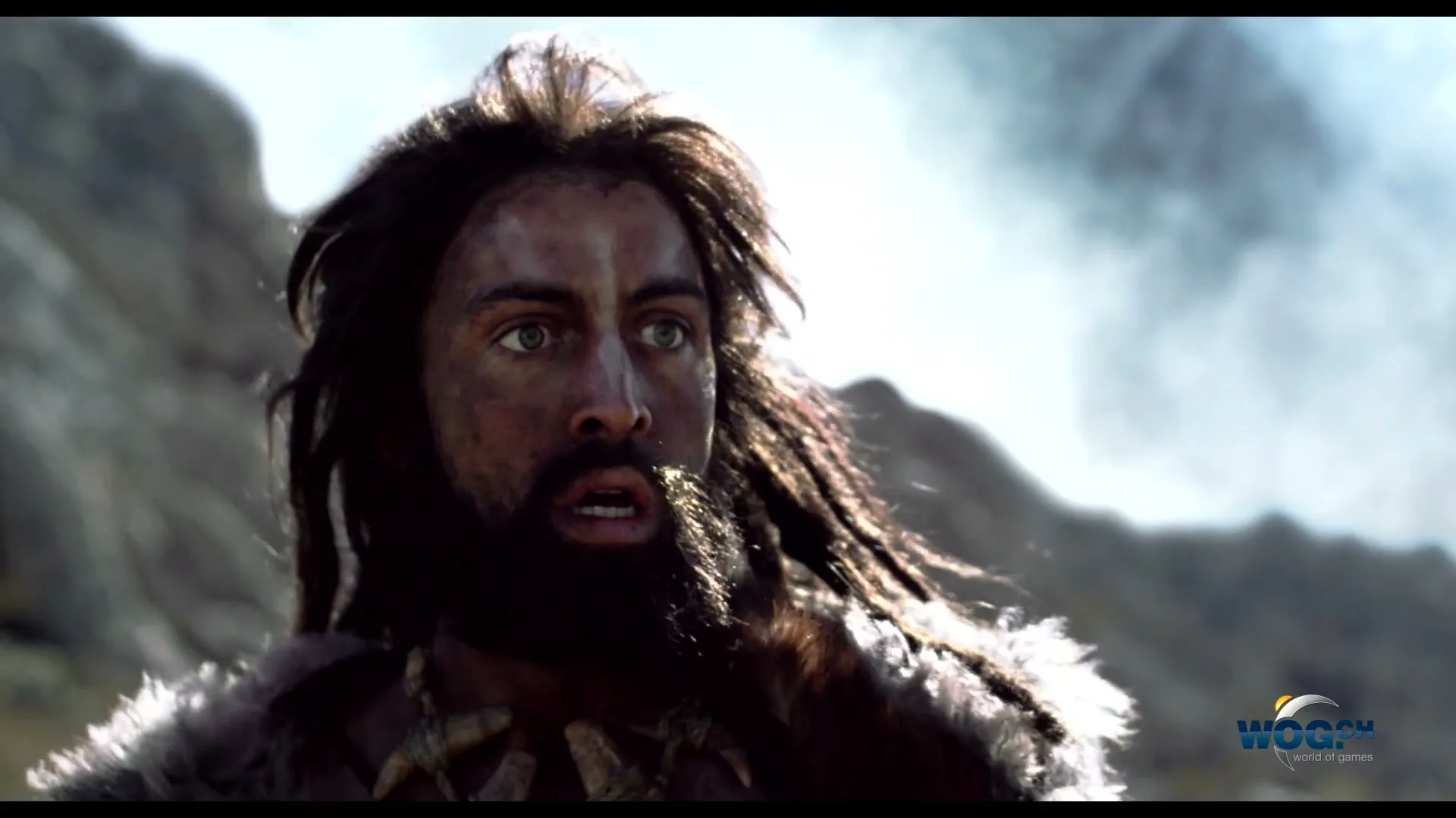 A man with long dark hair and a beard, wearing fur and bone necklace, looks up in fear in a rocky, smoky landscape.