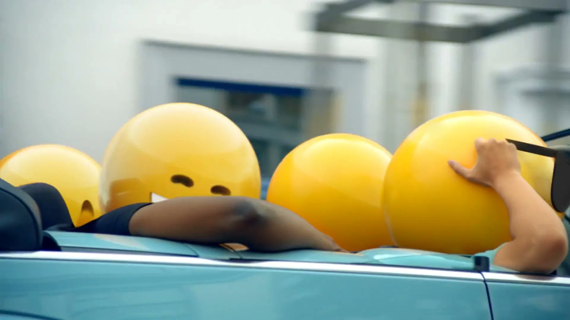 A group of people with emoji heads are riding in a convertible car, passing by a building with a "CREPERIE" sign.