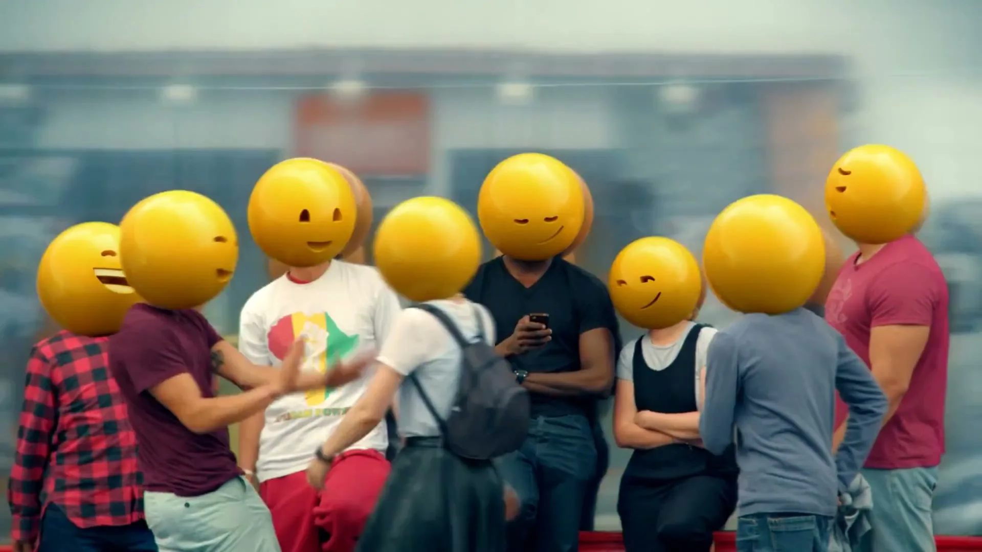 A group of young people with emoji heads are standing and interacting on a city street, with reflections of buildings in the background.