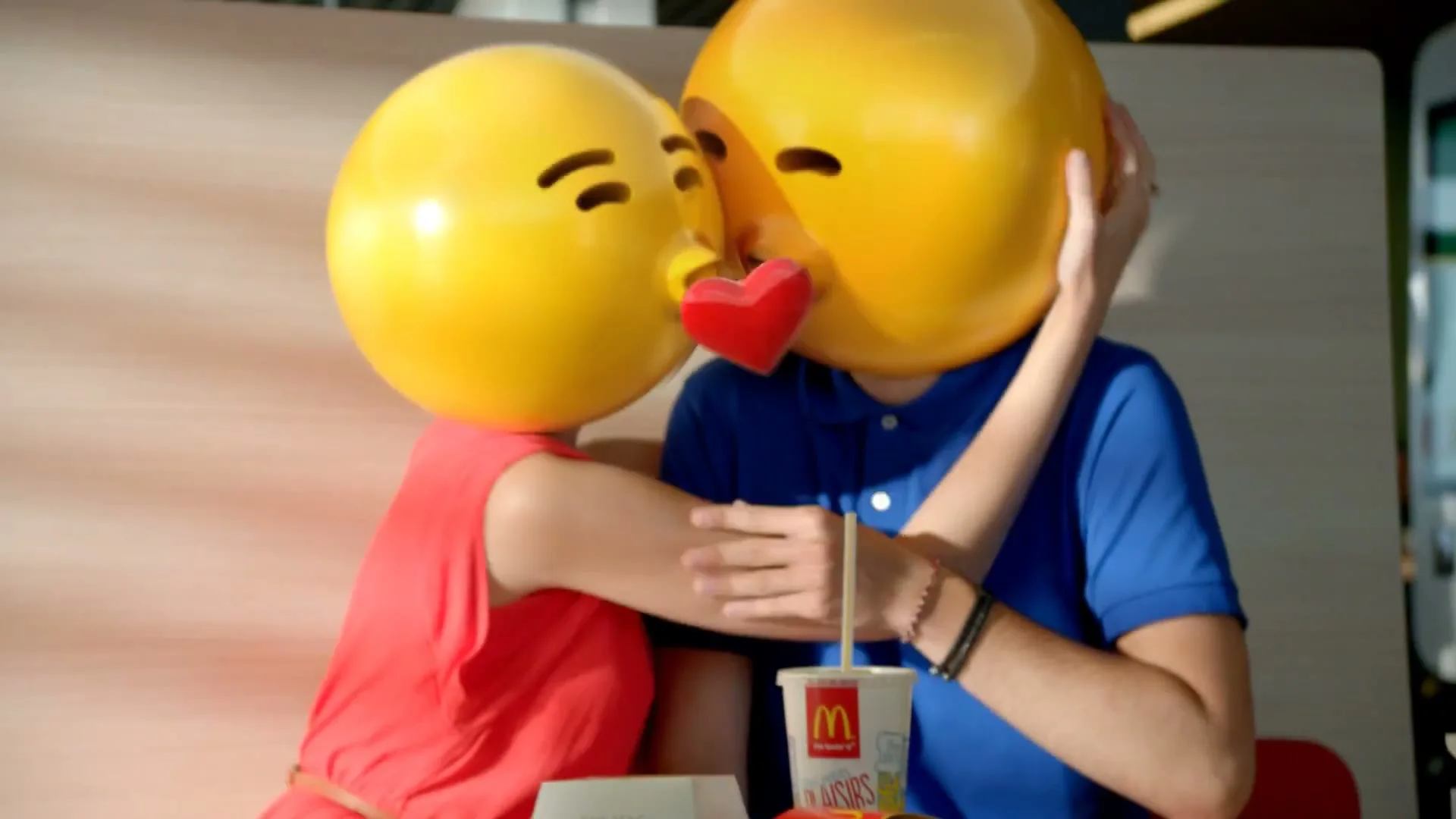 A couple with emoji heads kiss at a McDonald's table, then look surprised, with a Big Mac and fries on the tray.