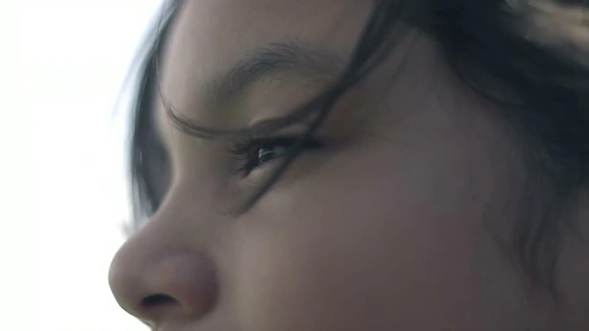 A young person's face is shown in profile, with their eye looking intently forward, hair blowing slightly in the wind.