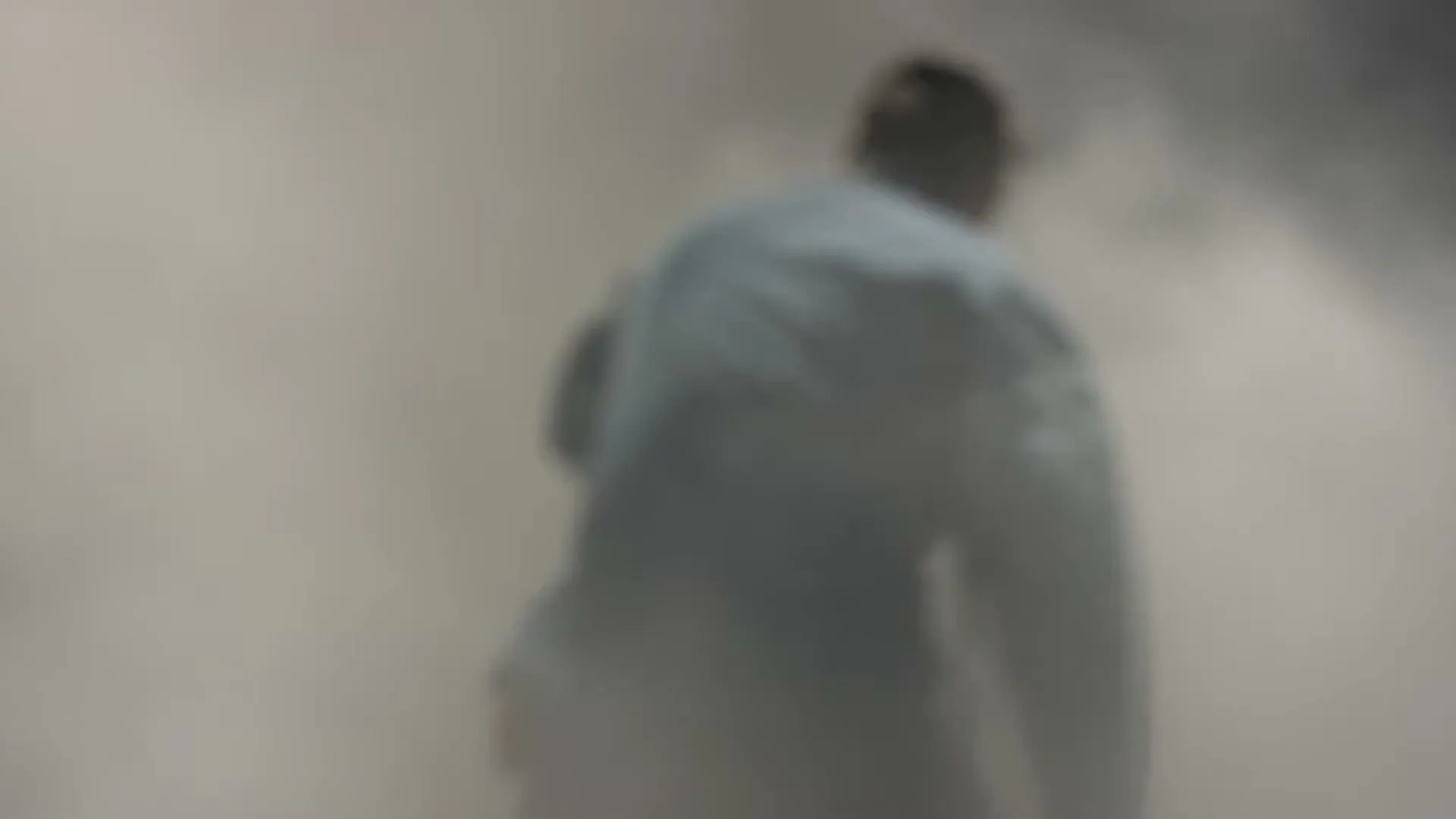 A blurry shot of a person in light-colored clothing, seen from behind, walking through a cloud of dust or smoke.
