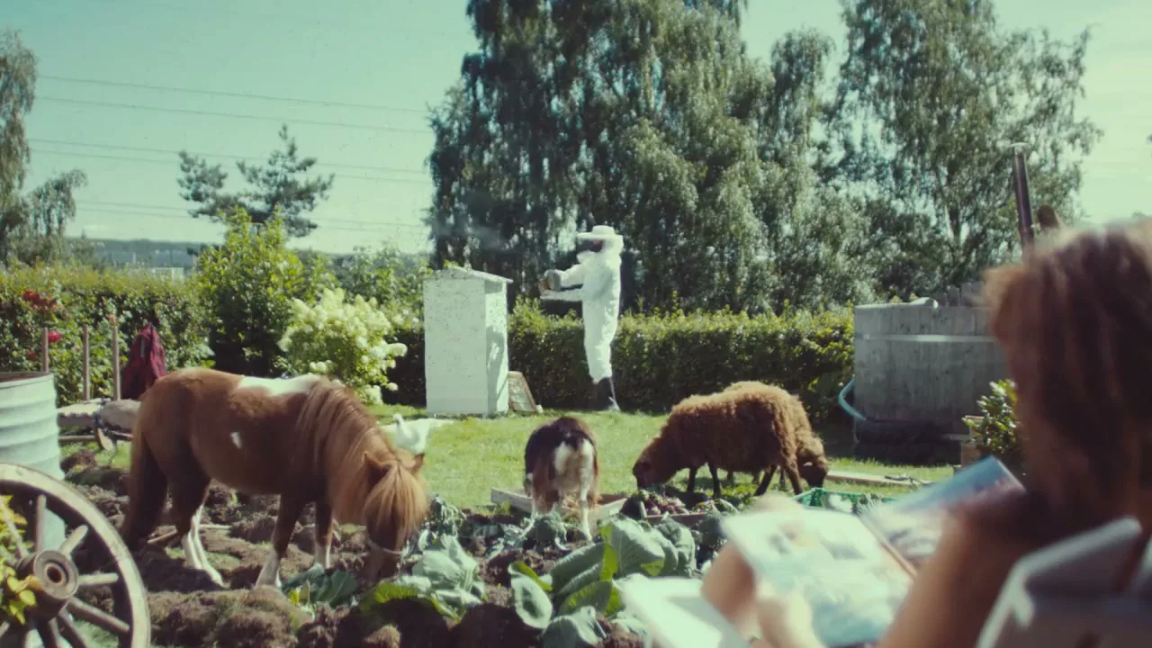 A person in a beekeeper suit tends to a beehive in a backyard garden, while a pony, a sheep, and a dog graze nearby.