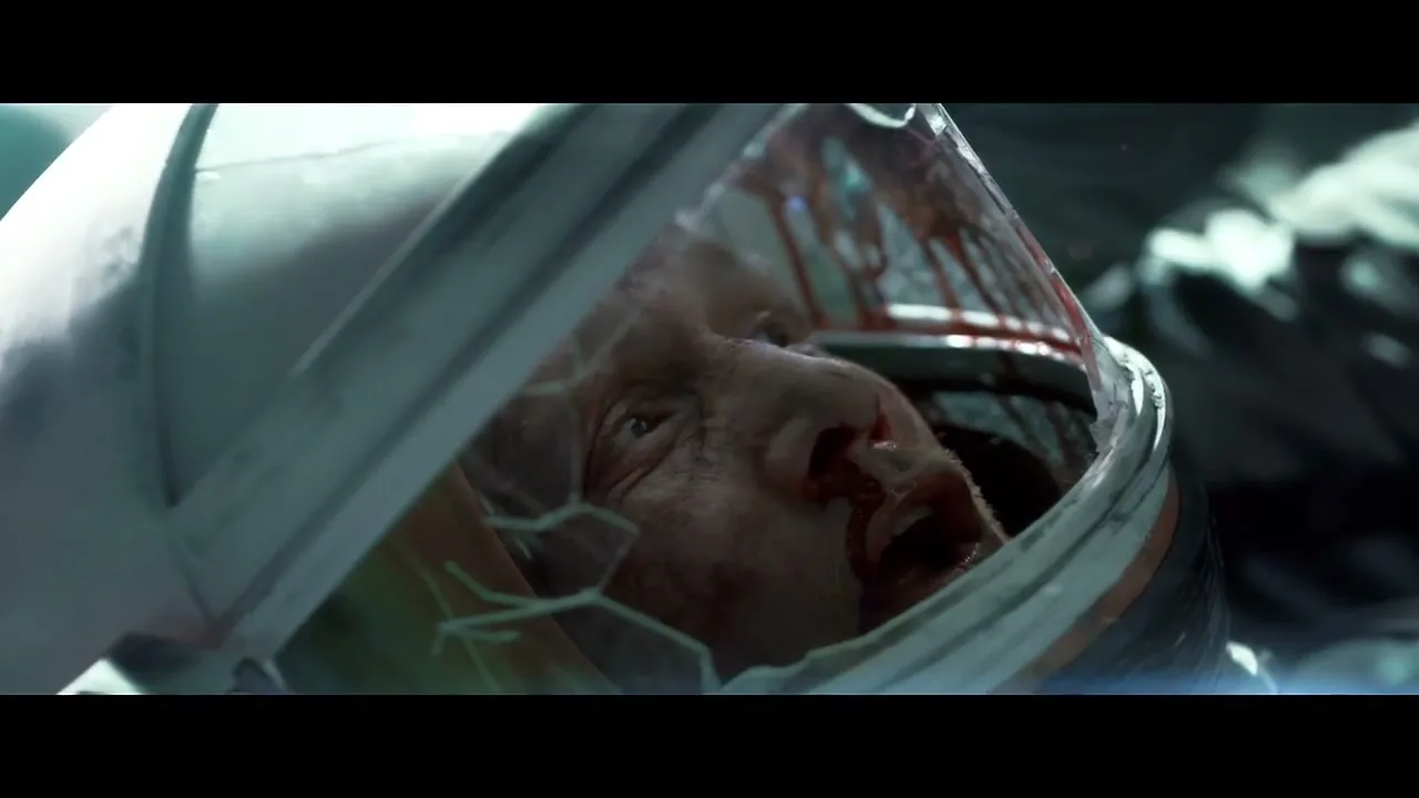 A male astronaut with a bloody face and a cracked helmet is seen in a medium closeup shot, looking upwards in distress.