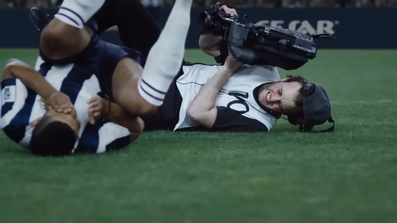 A cameraman and a soccer player are tangled on the ground after a collision on a soccer field.