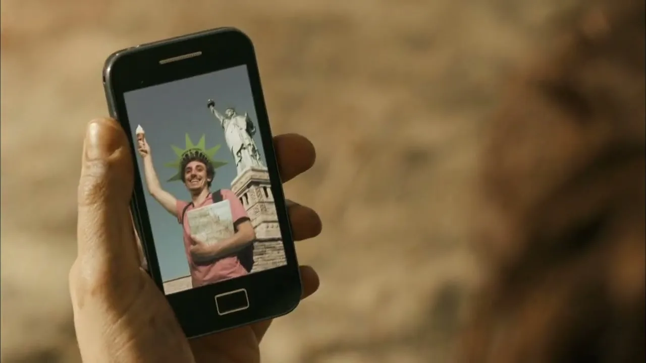 A person's hand holds a smartphone, swiping through photos of a young man posing in front of New York City landmarks.