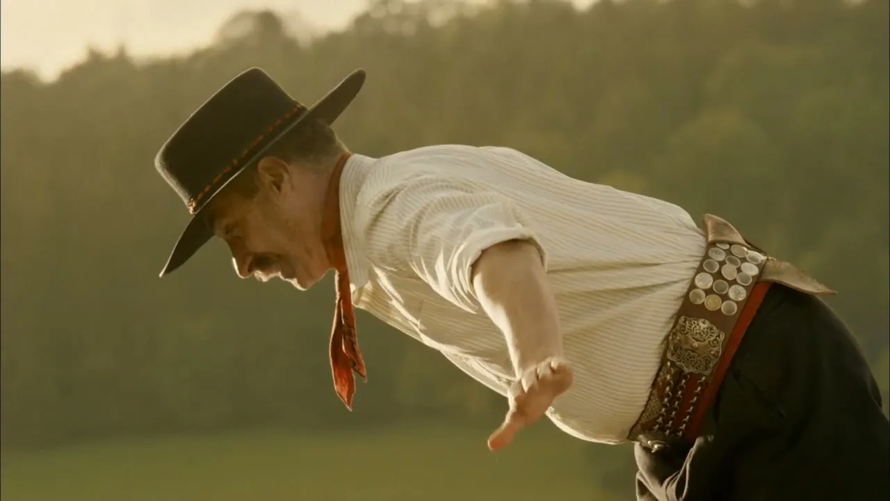 A man in a gaucho hat and traditional attire leans forward, then slowly rises with arms outstretched, in a sunlit field.