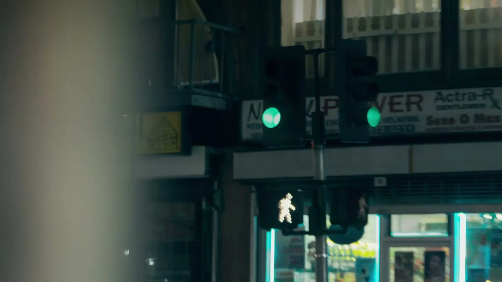 A traffic light changes from red to green, with a pedestrian signal also changing, on a city street at night.