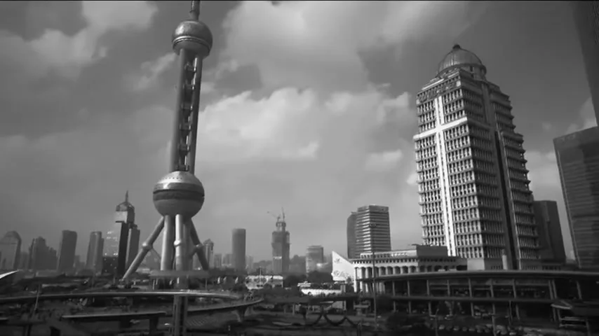A wide shot of the Shanghai skyline in black and white, featuring the Oriental Pearl TV Tower and other tall buildings under a cloudy sky.