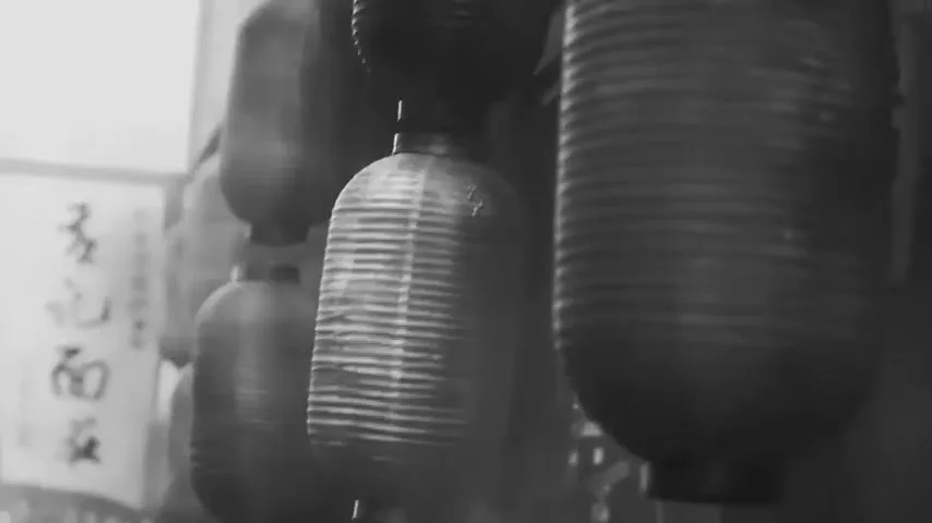 A close-up, black and white shot of traditional Japanese lanterns hanging in a row, with some blurred in the background.