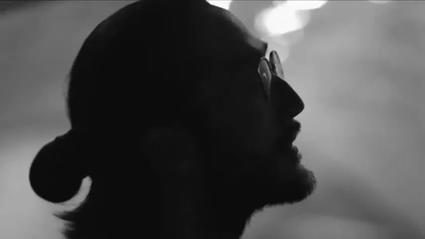 A man in silhouette with a beard and glasses looks up, with blurry lights in the background.