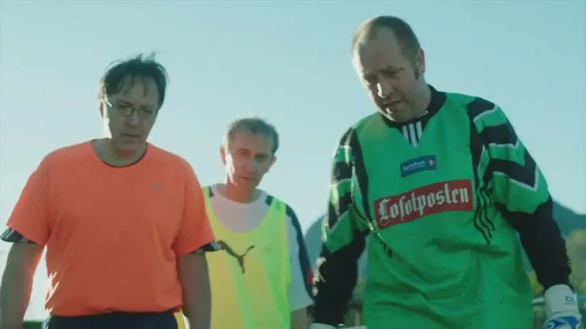 Three middle-aged men in soccer jerseys walk across a sunny outdoor field, looking downcast after a game.