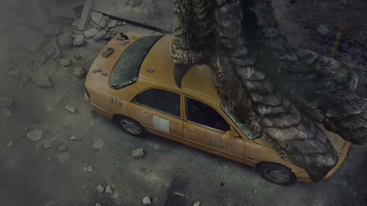 A giant monster's foot crushes a yellow taxi cab on a debris-strewn street in a destroyed city.
