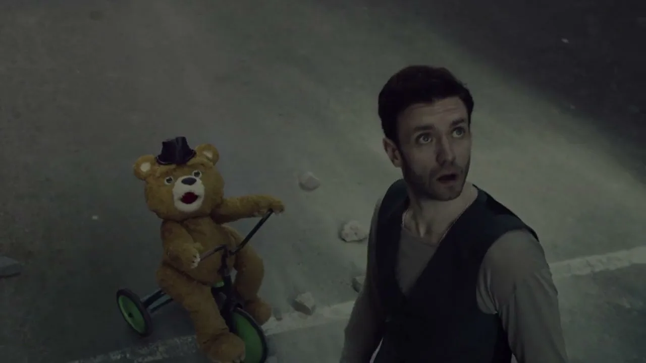 A man in a vest and a teddy bear on a tricycle look up in surprise on a dark, empty street.