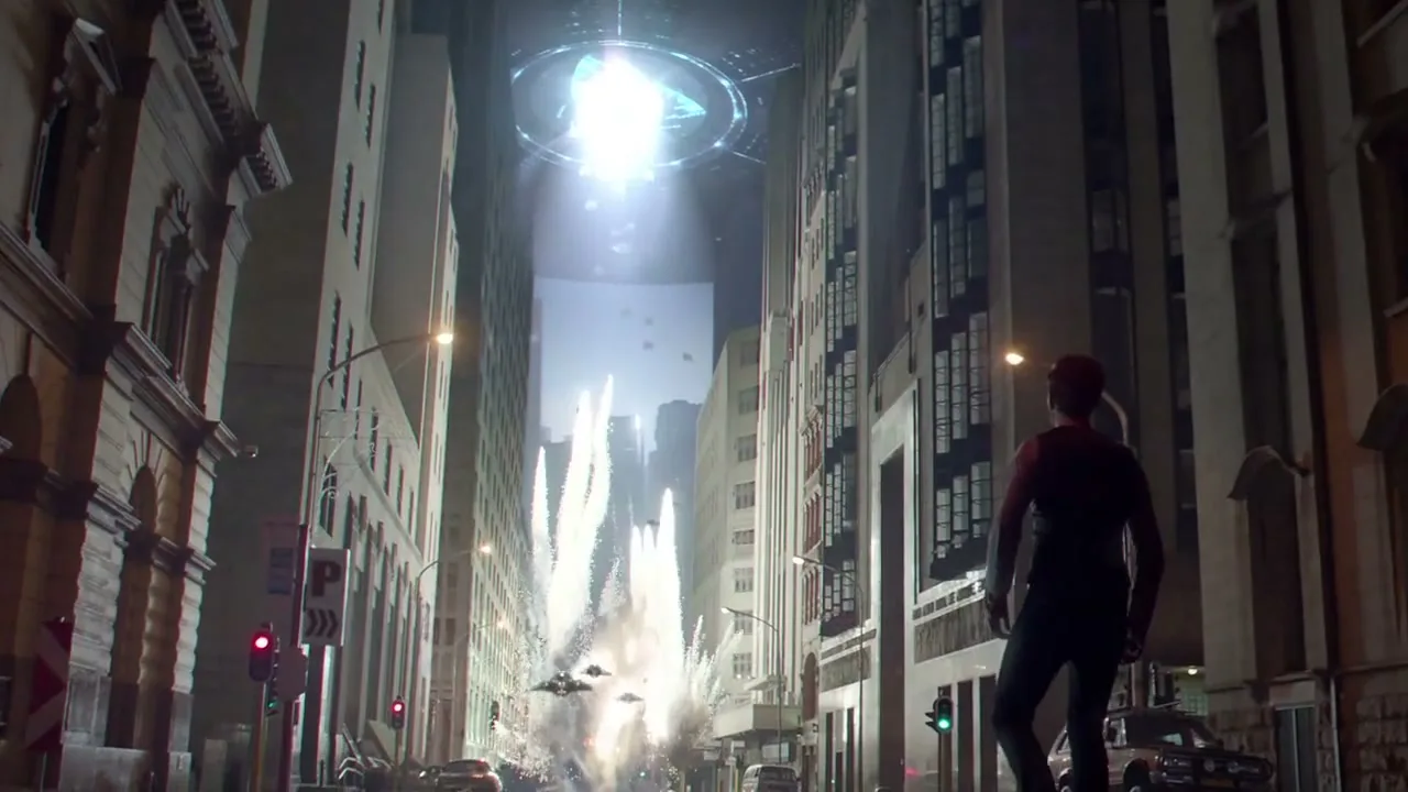 A man in a dark outfit stands on a city street at night, looking up at a giant glowing alien spaceship hovering between tall buildings, as explosions erupt below.