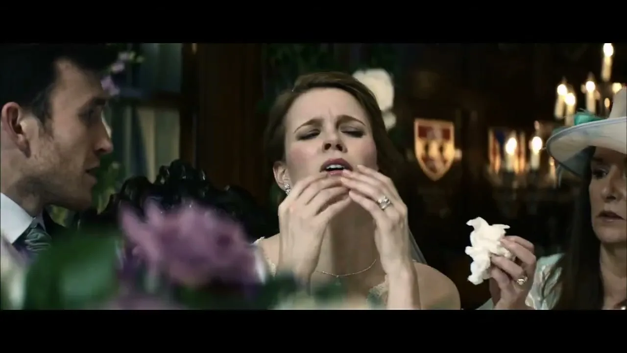 A bride in a white dress is about to sneeze, with a man and woman looking on in a dimly lit interior.