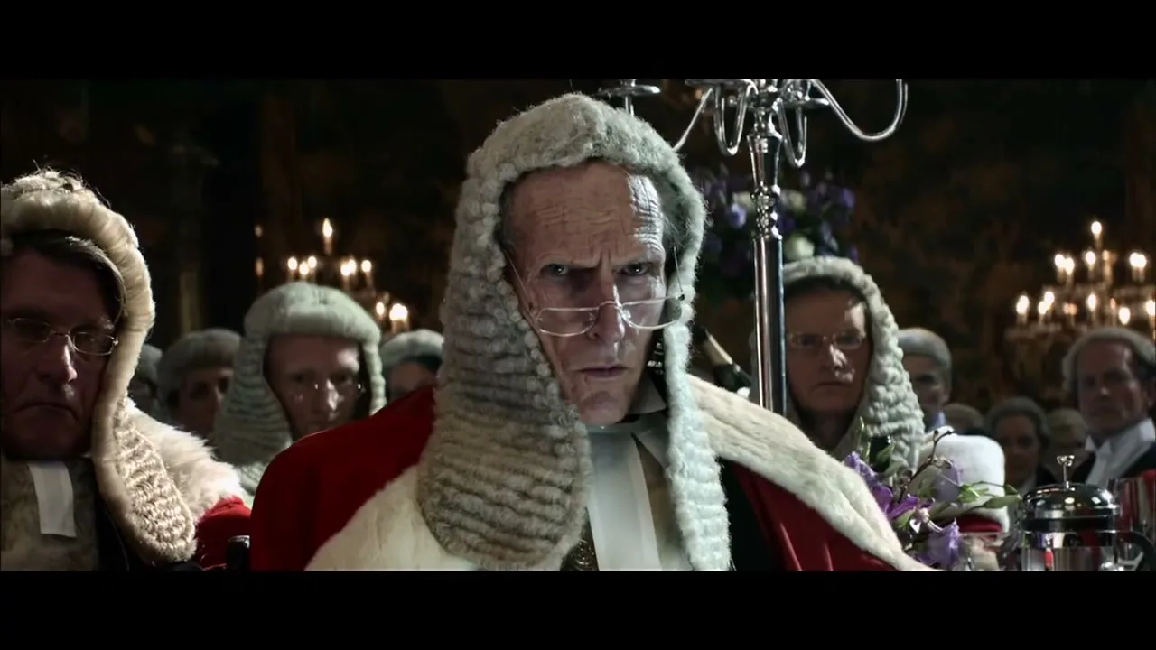 A stern-looking judge in a wig and red robes stares directly at the camera in a candlelit hall, surrounded by other judges.