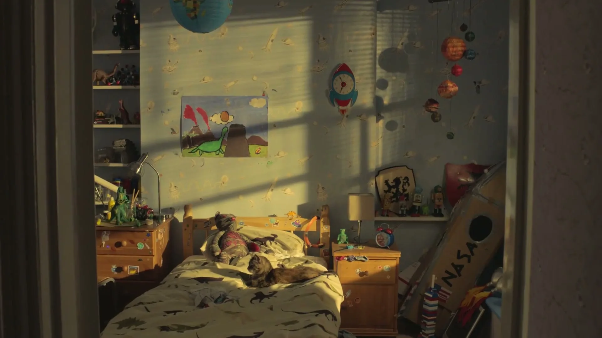 A wide shot of a child's bedroom, filled with toys and a bed where a cat is sleeping, with sunlight streaming through the window.