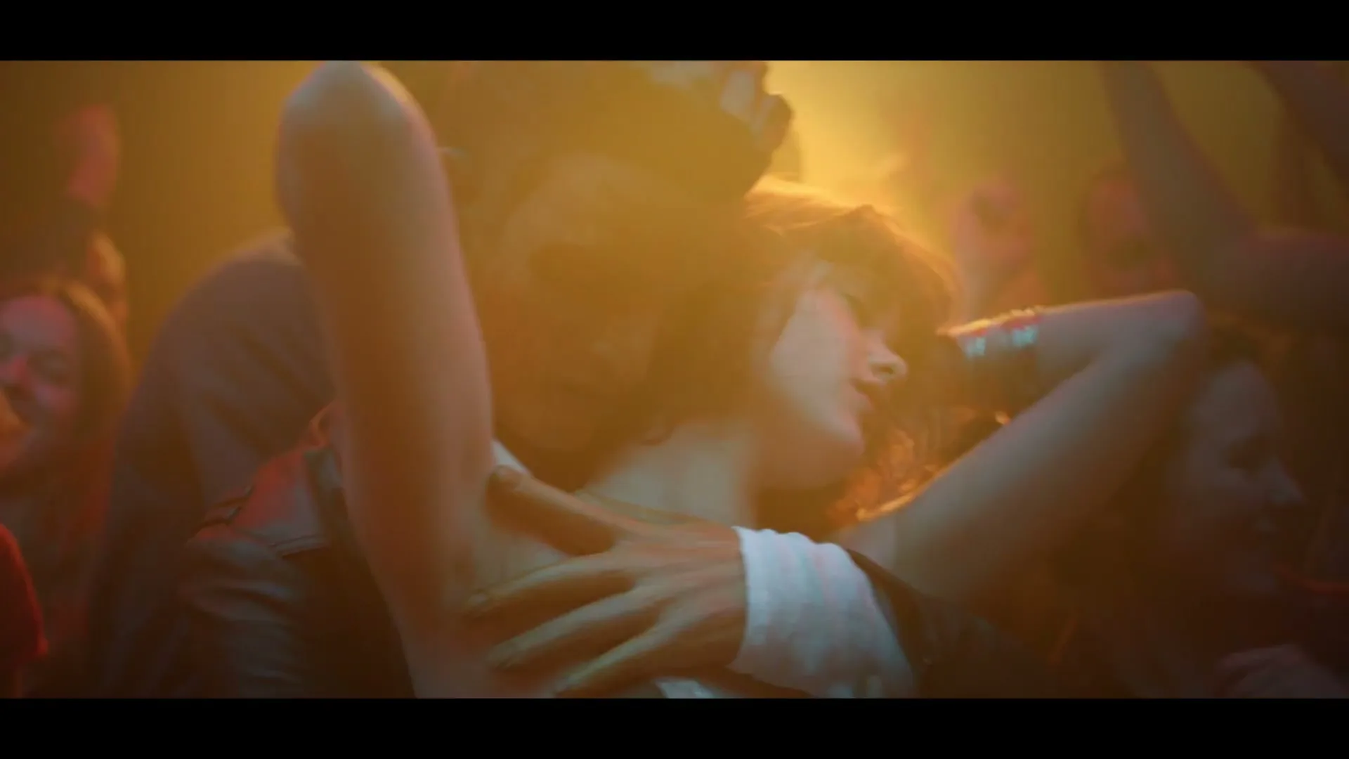 A young woman with dark hair dances closely with a man in a Woody costume at a crowded, dimly lit nightclub.