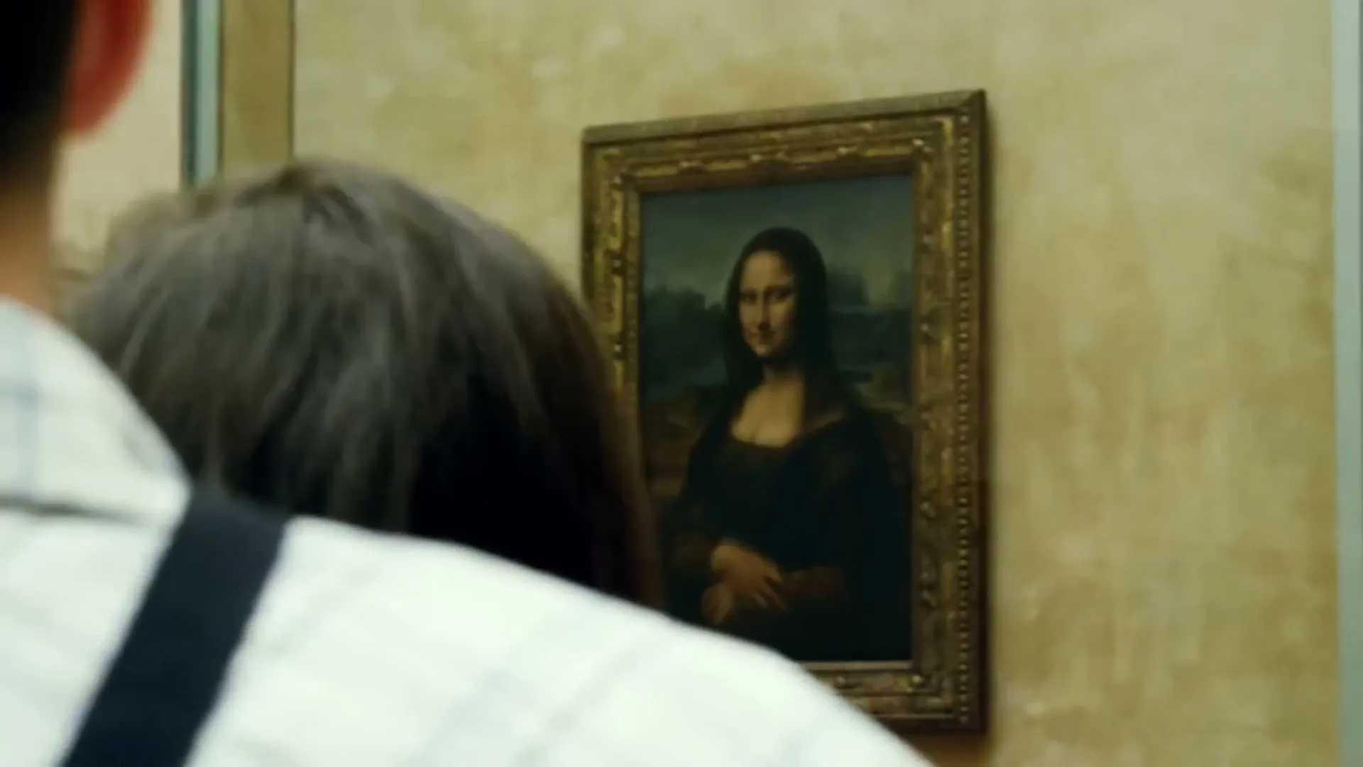 Two people with their backs to the camera look at the Mona Lisa painting in a museum.