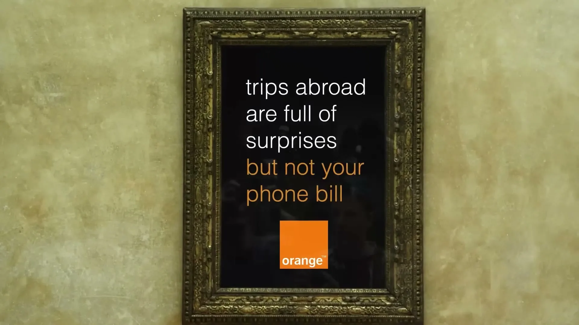 A framed painting with a dark canvas and white text, then orange text, then an orange logo, is centered on a textured wall.