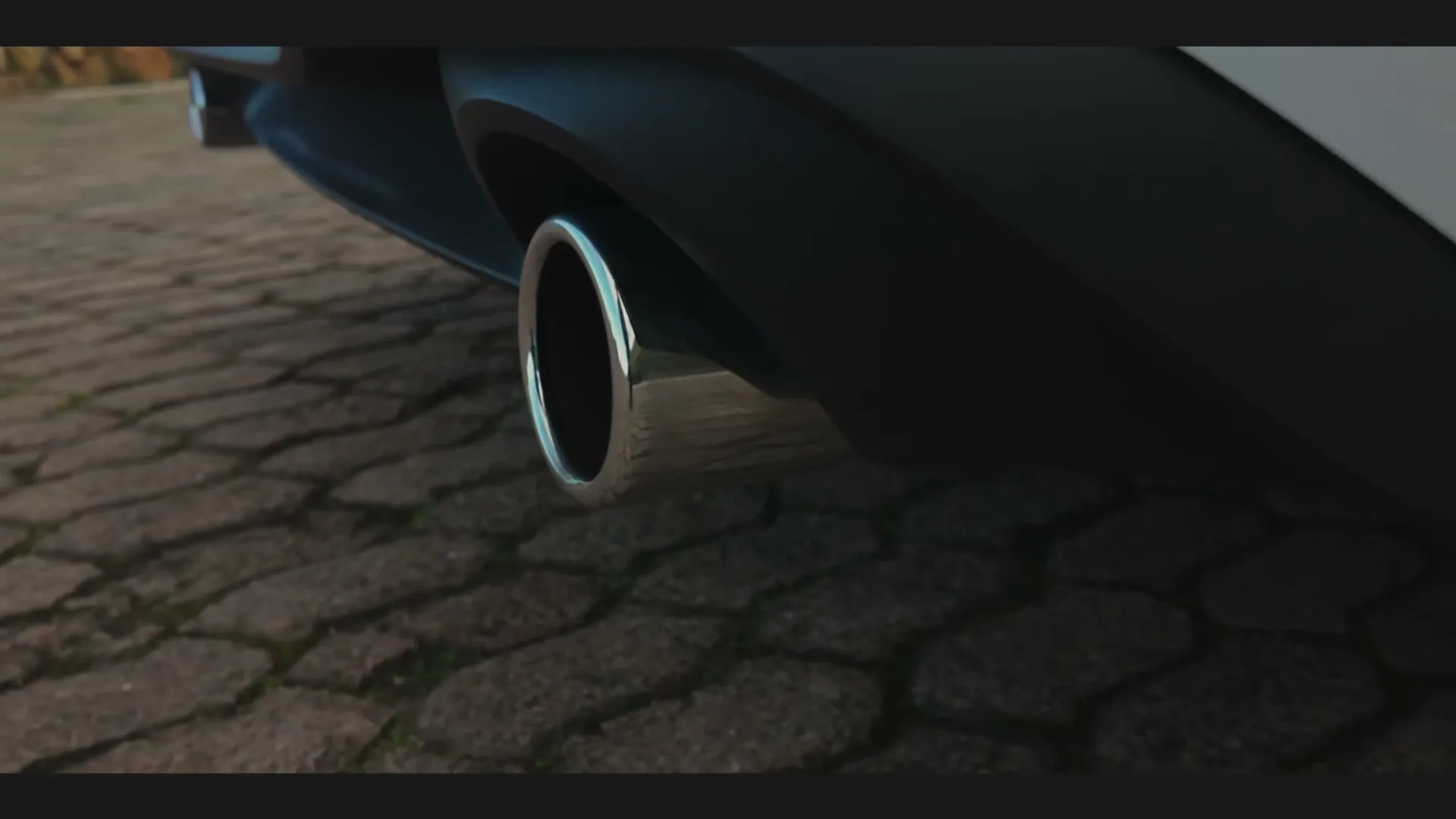 A close-up shot of a car's exhaust pipe, showing its chrome finish and the textured ground beneath it, with a slight camera movement.