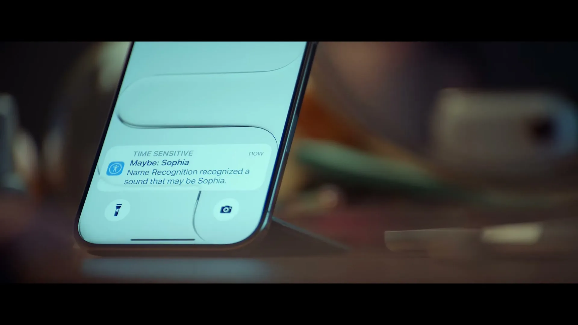 A close-up shot of an iPhone displaying a "Time Sensitive" notification for "Maybe: Sophia" on a wooden surface.