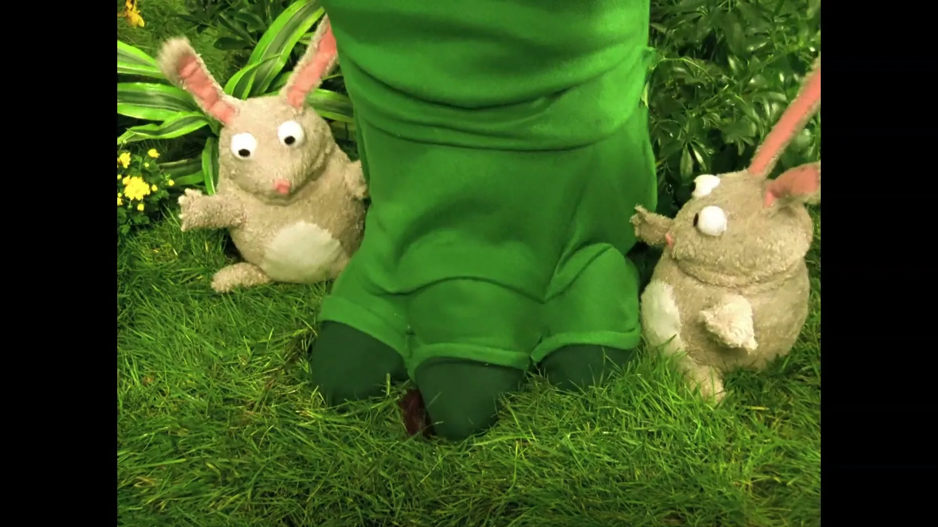 Two rabbit puppets and a frog puppet are sitting in green grass, then a large green monster foot stomps down between them.