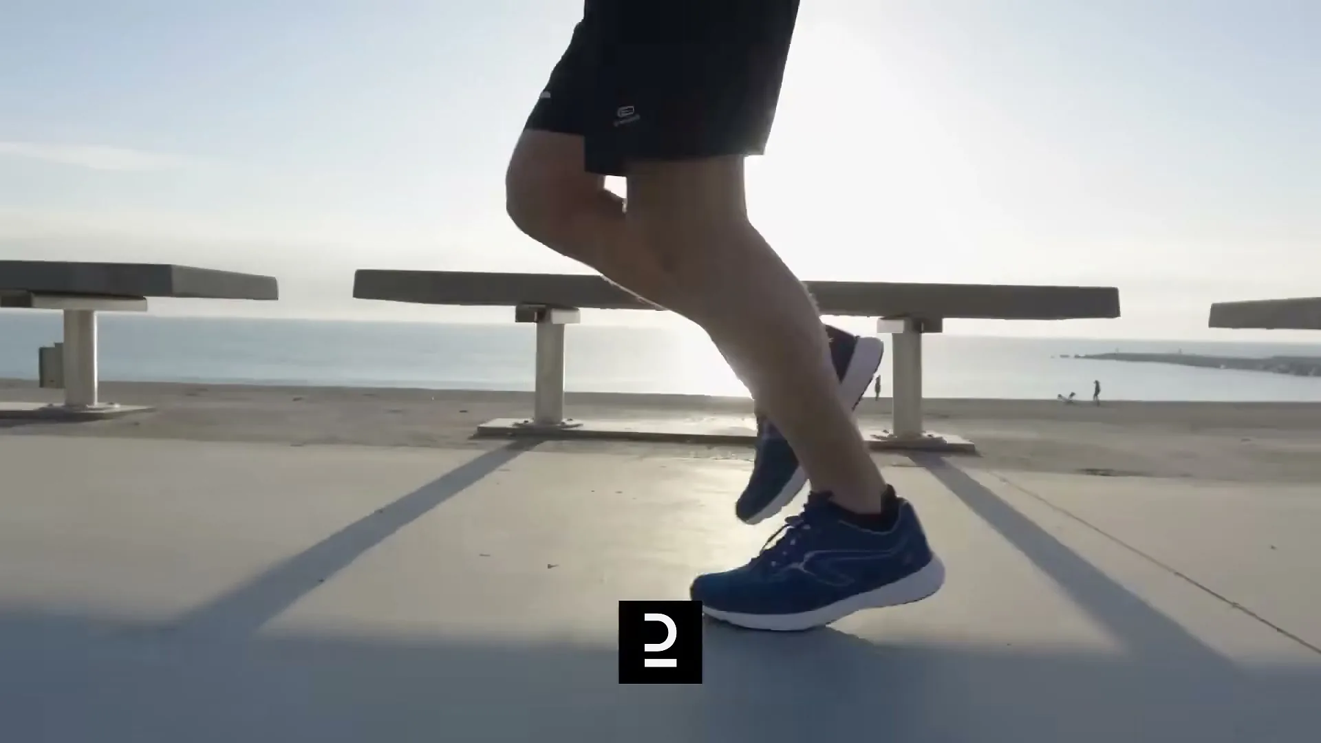 A person's legs and feet are shown running on a concrete surface with the ocean and bright sun in the background.