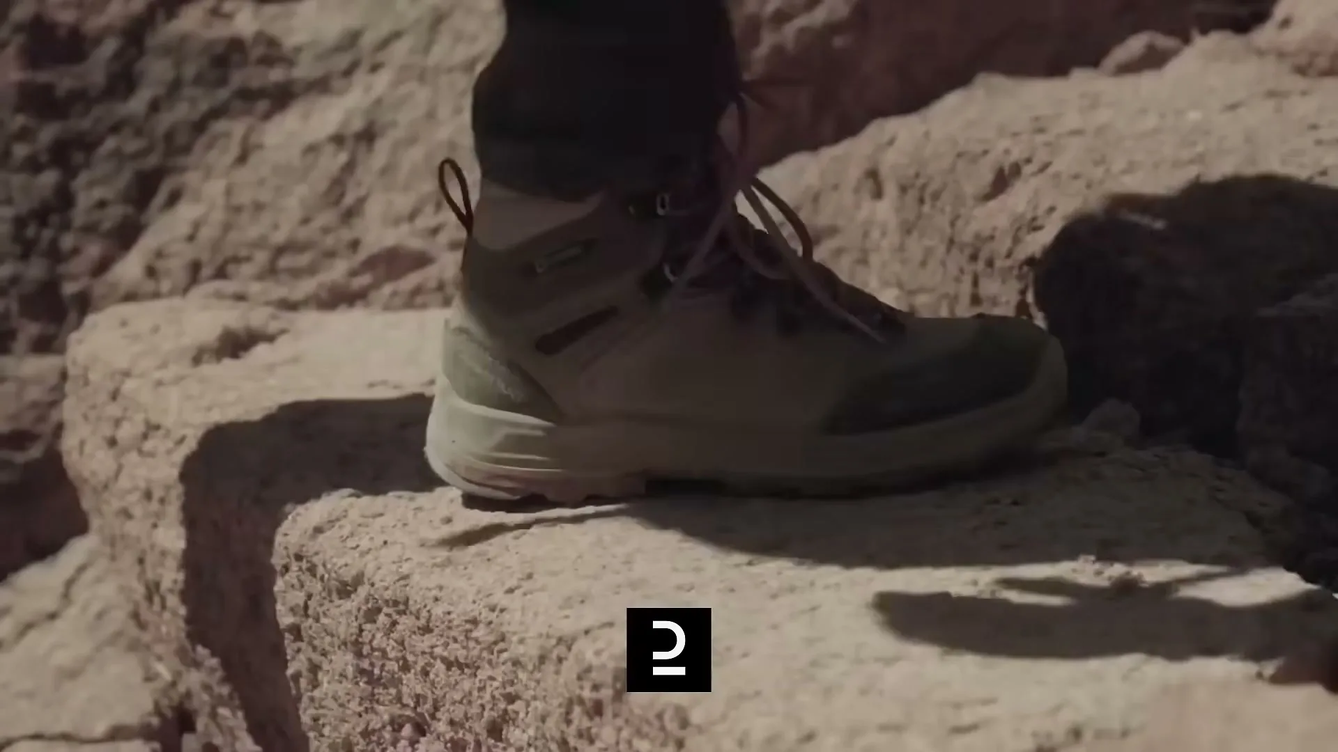 A person's foot in a hiking boot steps onto a rocky surface in a desert landscape, showcasing the footwear's grip and durability.