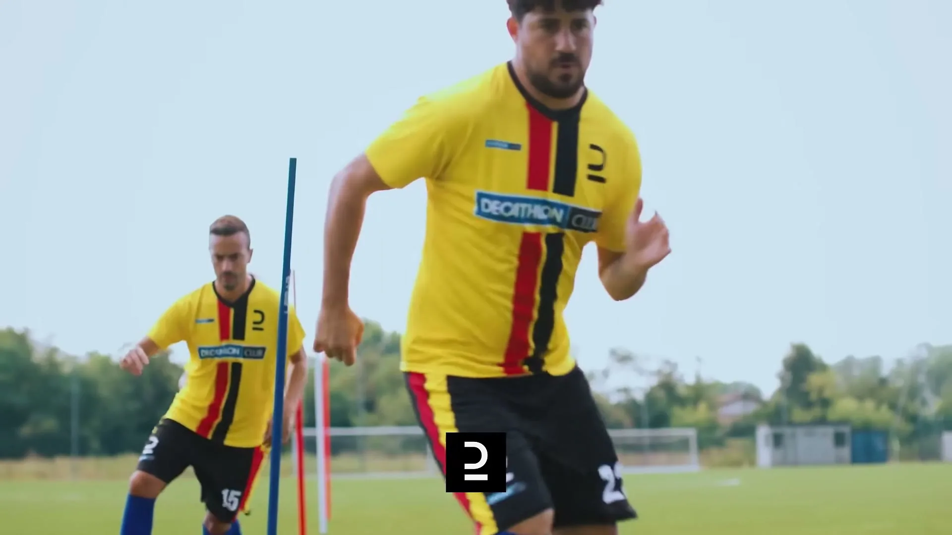 Three male soccer players in yellow and black jerseys run drills on a green field under a bright sky.