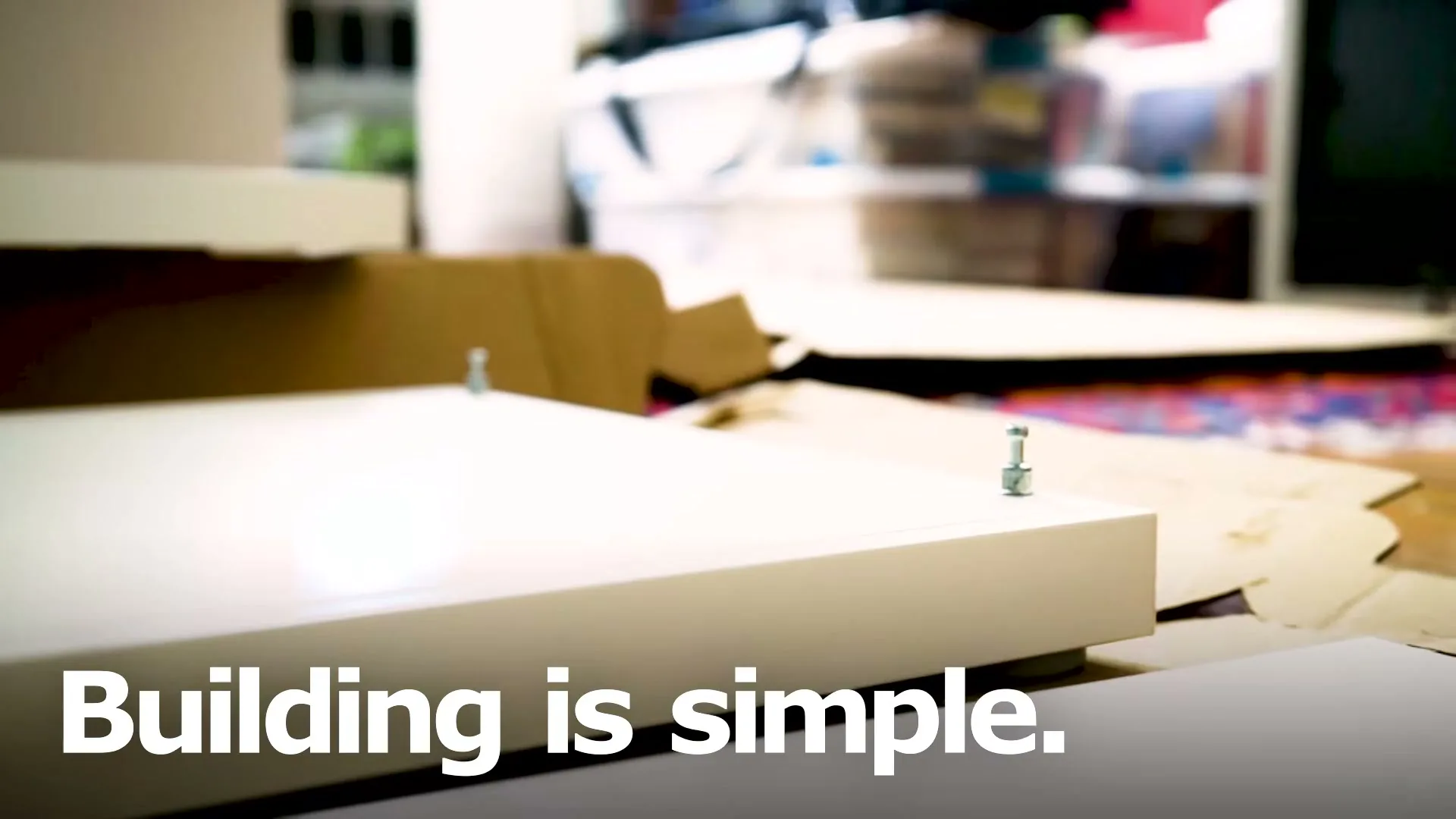 A close-up shot shows a white furniture panel with screws, surrounded by cardboard and other parts, with the text "Building is simple." overlaid.