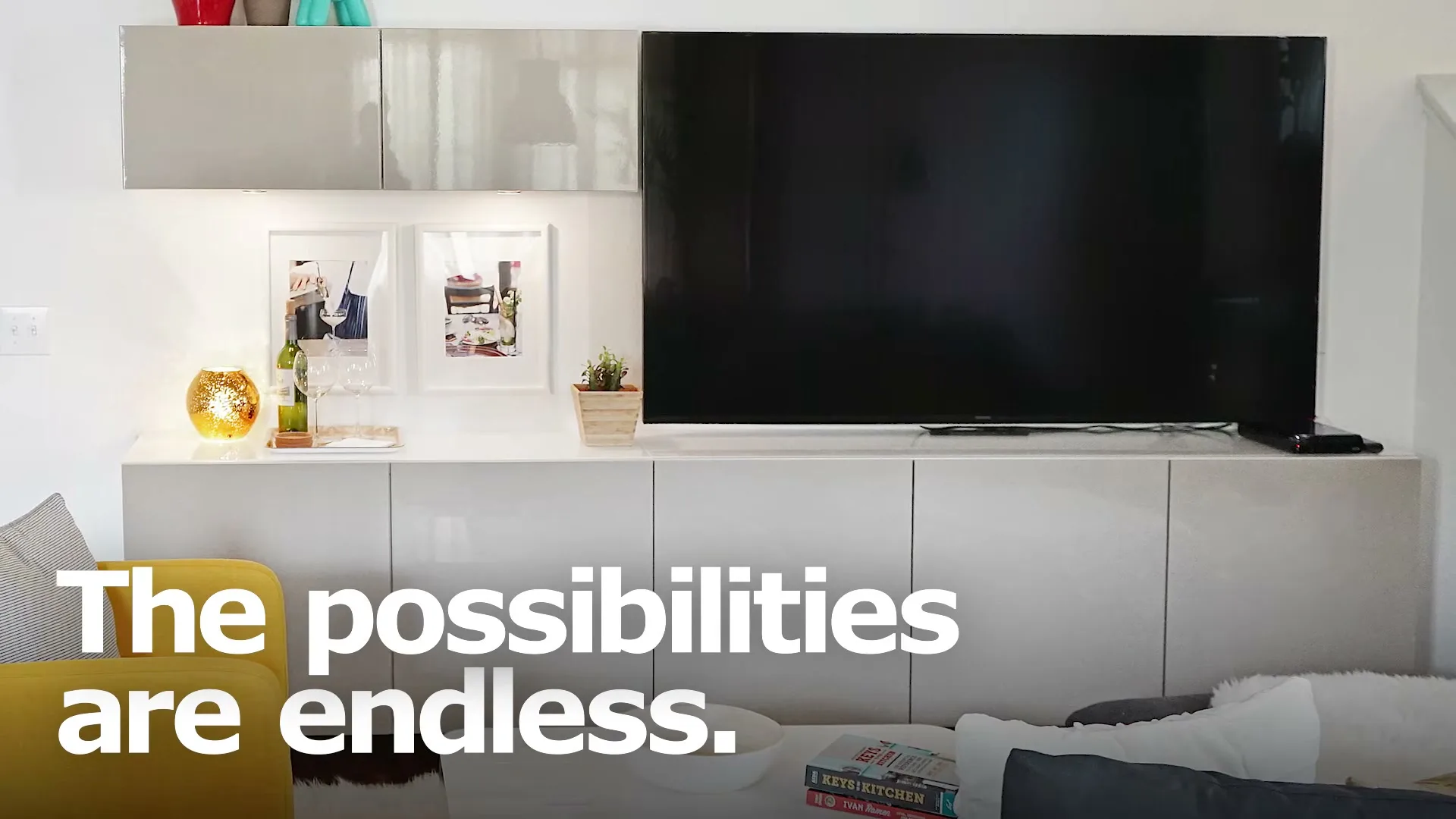 A wide shot of a modern living room with white cabinets, a large TV, and a yellow armchair, with text overlayed.