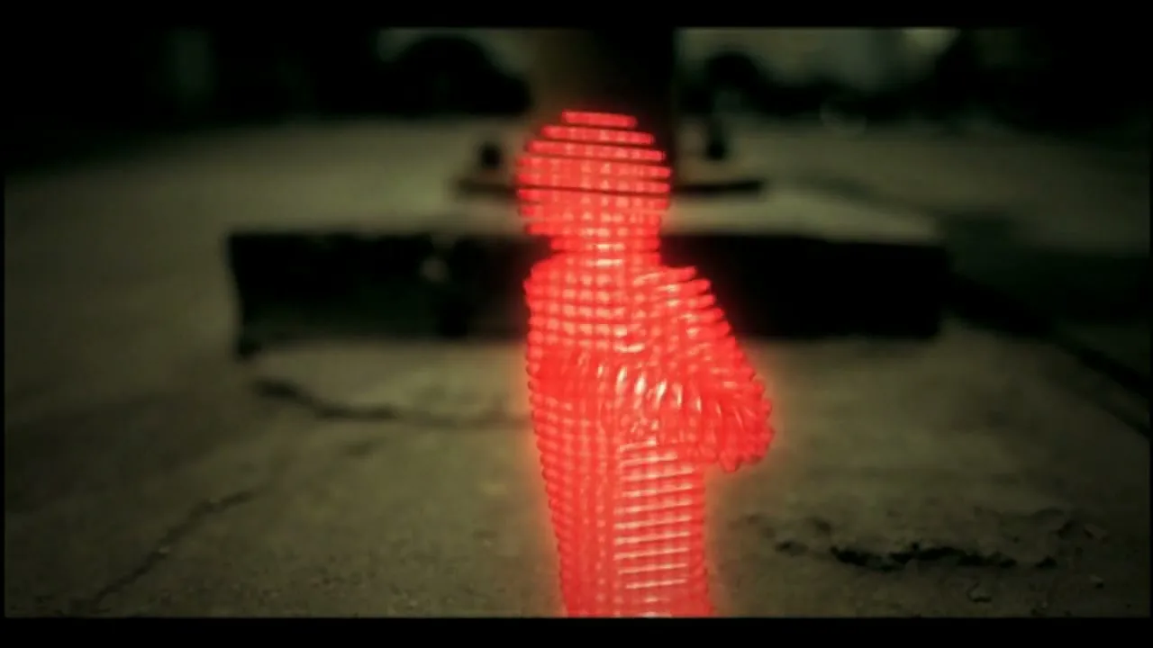 A red, pixelated, humanoid figure dances in a dark, industrial setting, with blurred machinery in the background.