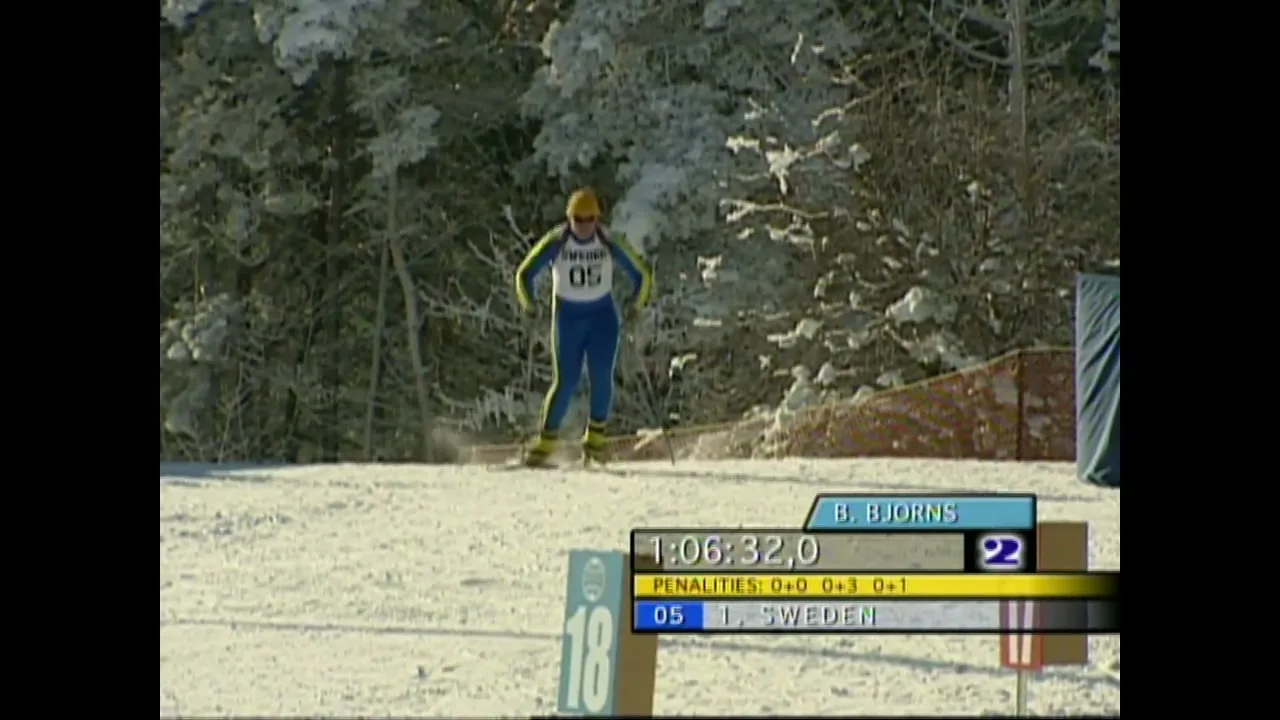 A biathlete in a blue and yellow suit skis across a snowy landscape with trees in the background, as on-screen graphics display race information.