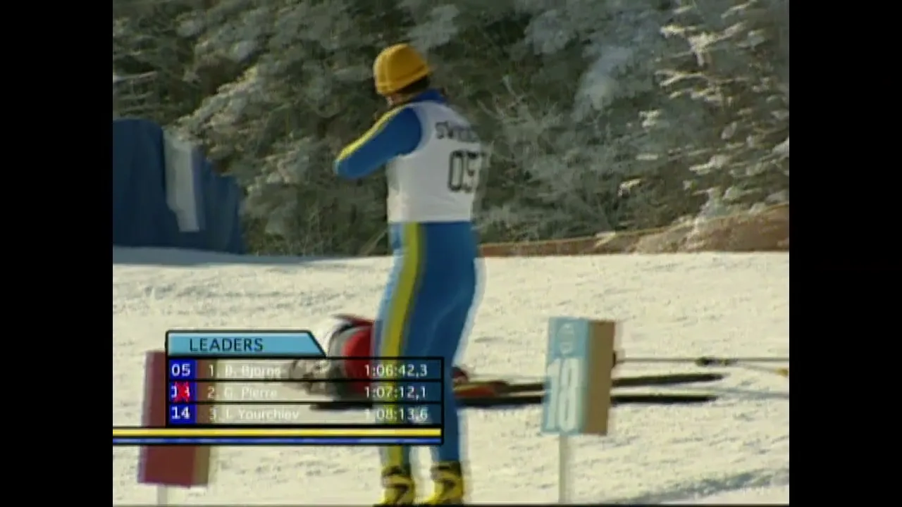 A biathlete in a yellow hat and blue and yellow suit shoots a rifle while another biathlete in black and red falls in the snow at a snowy outdoor biathlon course.