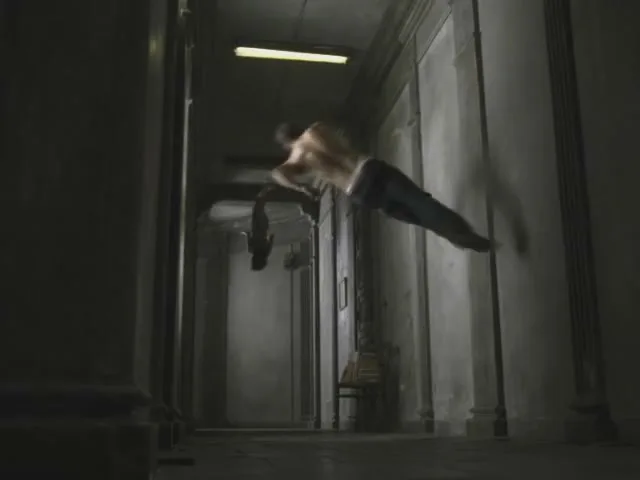 A shirtless man in jeans floats horizontally through a dark, old, narrow hallway, seemingly pulled by an unseen force.