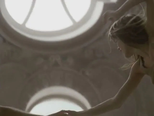 A man and woman, both shirtless, are seen in a blurry shot, reaching for a Coca-Cola Light can that falls through a circular opening in a decorative ceiling.