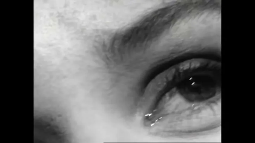 A black and white extreme closeup of a woman's eye, with a tear welling up, as she looks up.