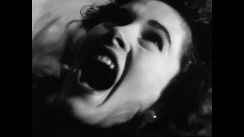 A woman with dark hair and an earring screams upwards in a dramatic black and white closeup shot.
