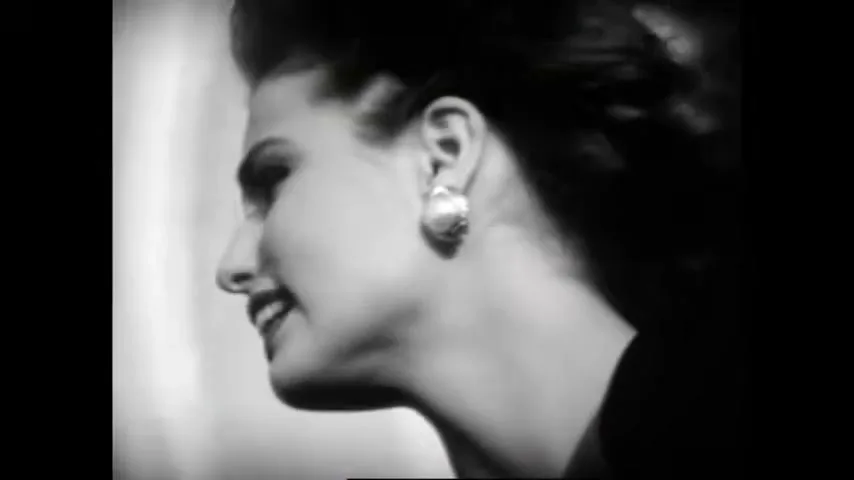 A beautiful woman with dark hair and pearl earrings looks up and screams in a dramatic black and white shot.