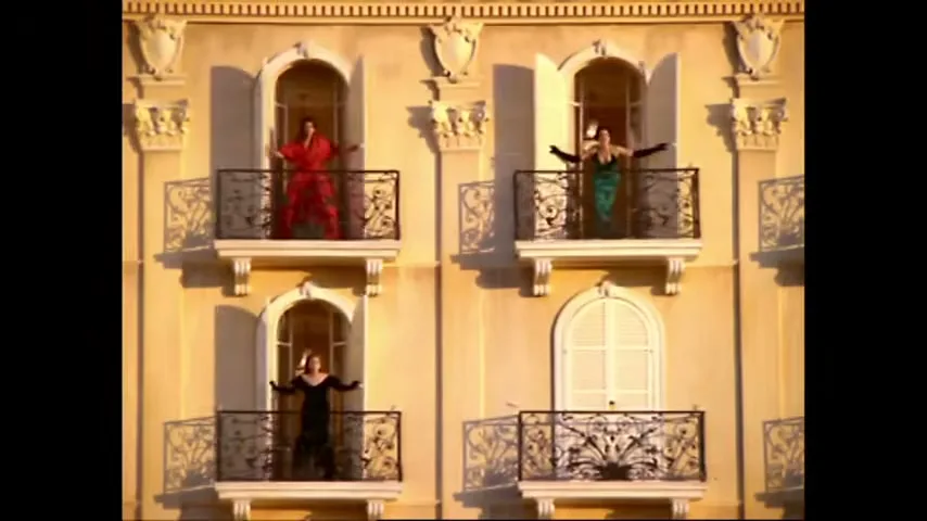 Three women in elegant dresses stand on balconies of a classical building, shouting and gesturing dramatically, then retreat inside as the shutters close.