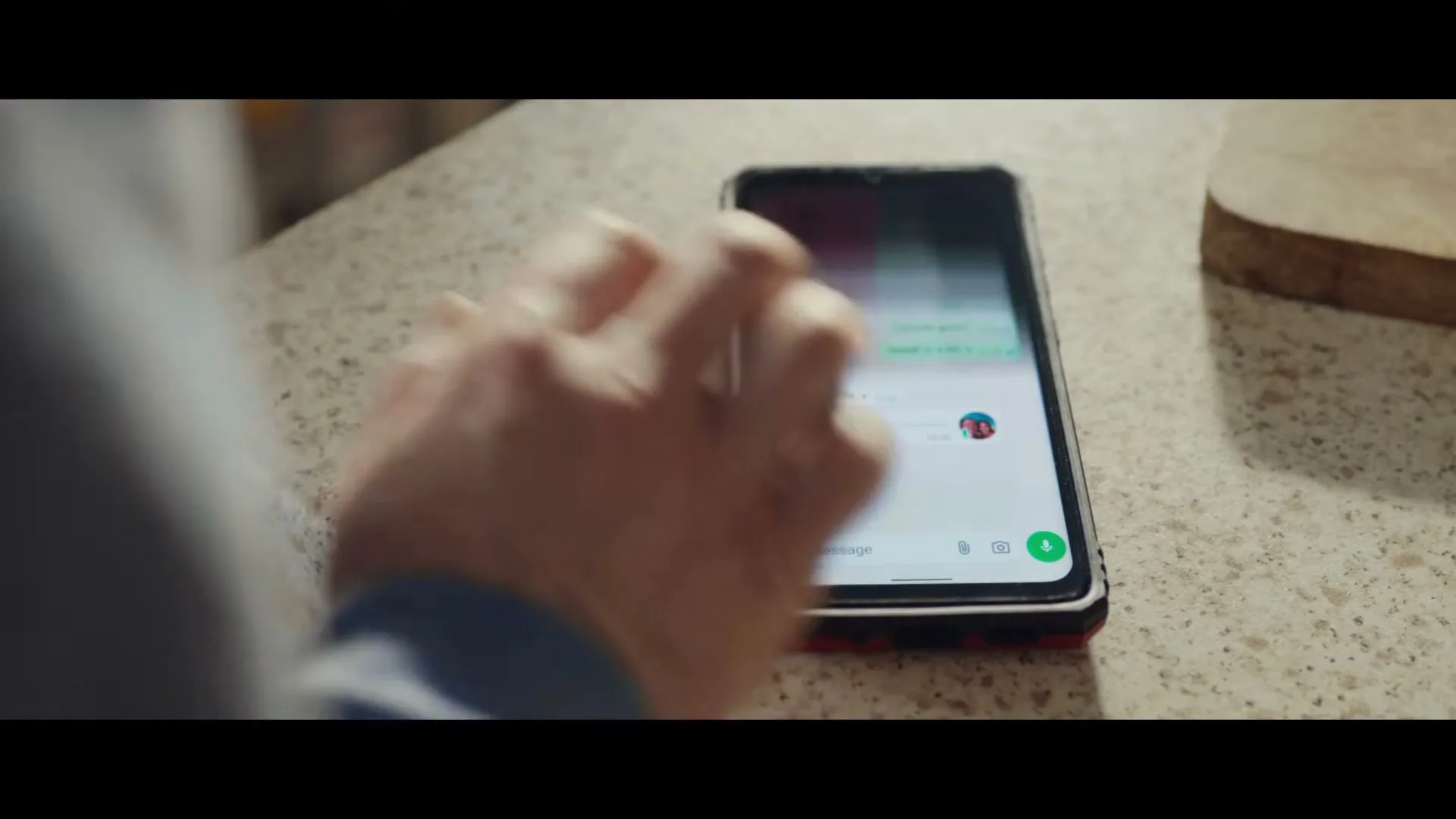 A person's hand taps on a smartphone lying on a speckled kitchen counter, revealing a WhatsApp chat with a contact named Rachel.