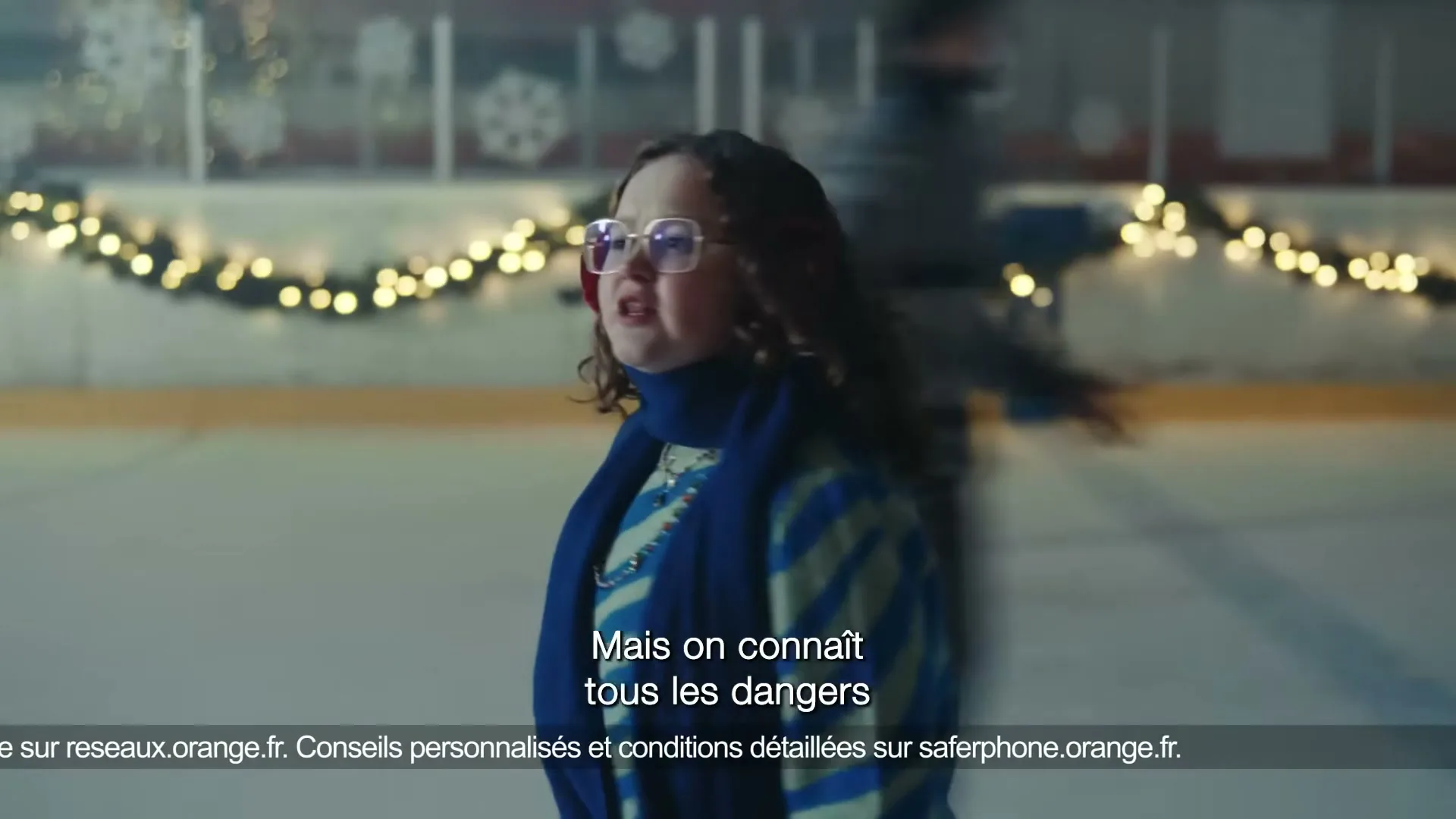 A young woman with glasses and a blue scarf skates on an ice rink decorated with string lights, looking around with a concerned expression.
