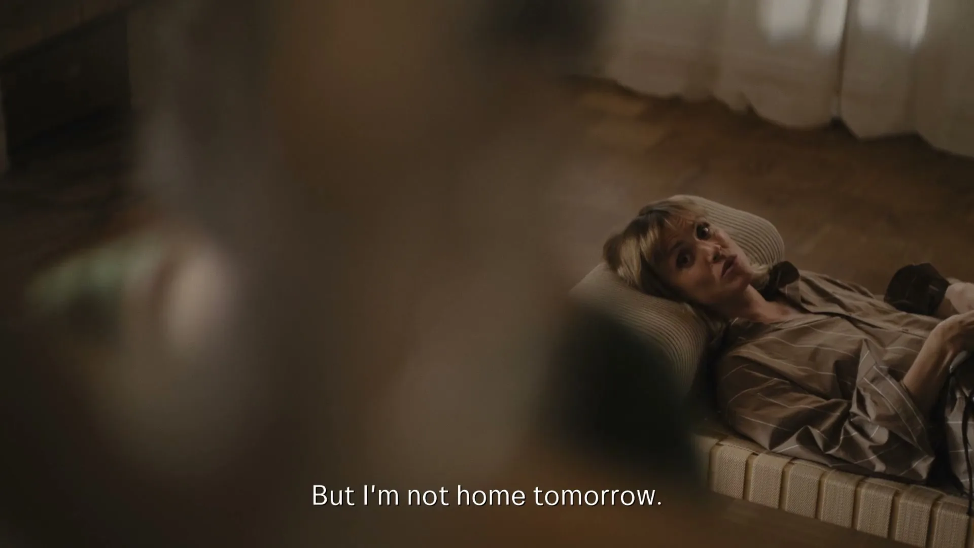 A woman in her 40s, wearing striped pajamas, lies on a daybed in a sunlit room, looking pensive.