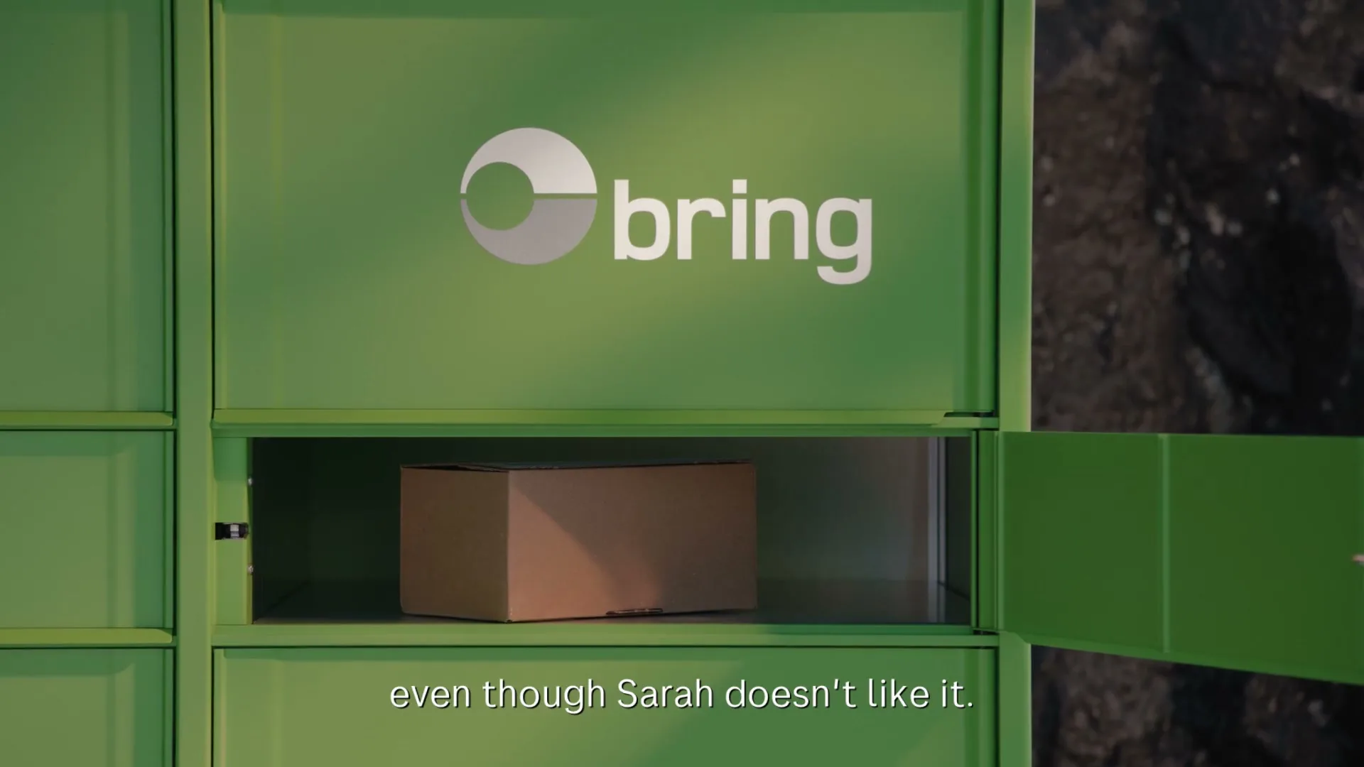 A green Bring parcel locker with the brand logo visible, opens to reveal a brown cardboard box inside, with text on screen.