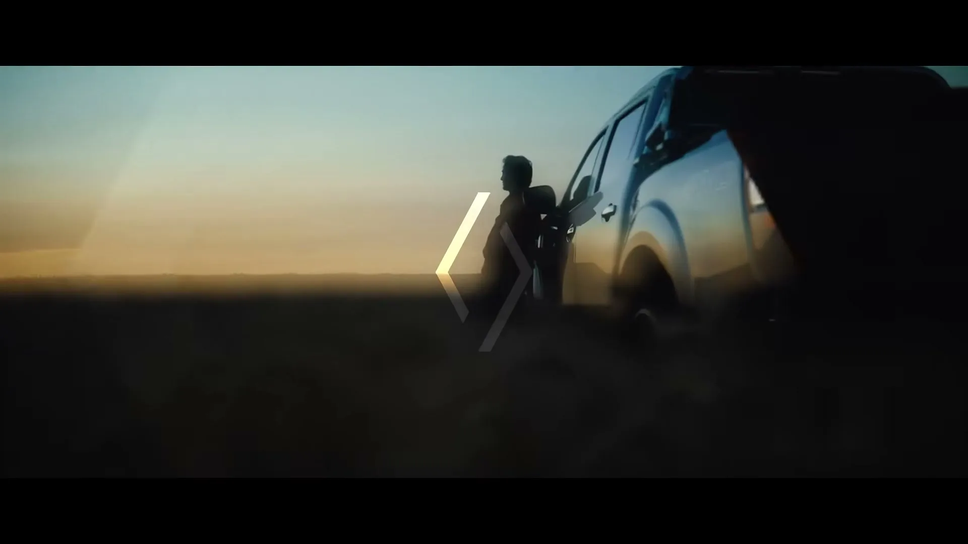 A man stands next to a pickup truck in a vast, open landscape at sunset, with the Renault logo subtly overlaid.